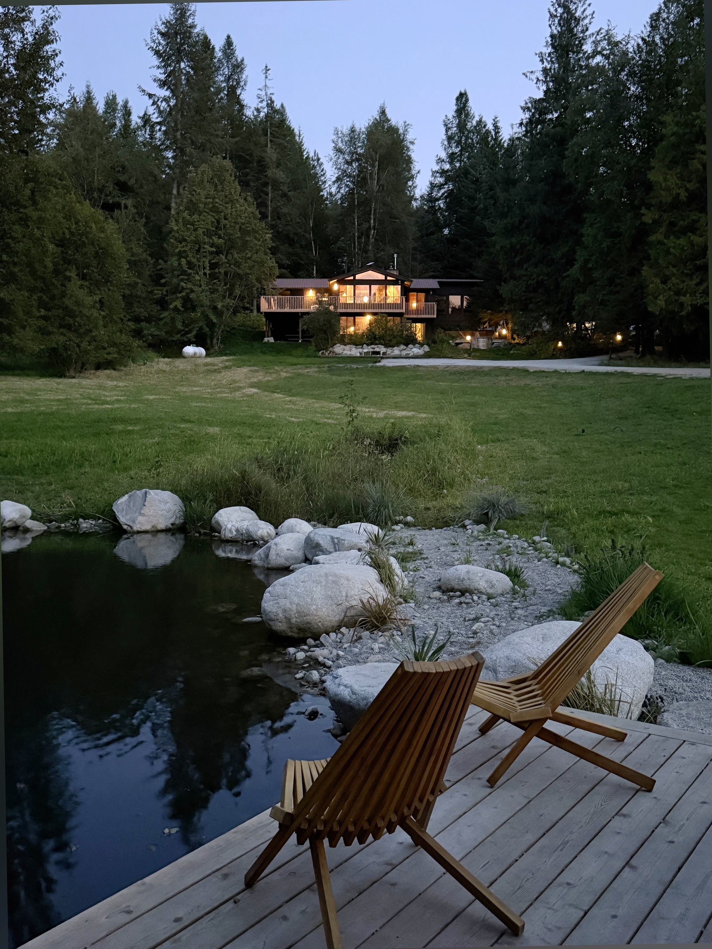 Dock chairs at dusk with the cabin lit up across the pond